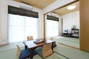 和室の居室。机と椅子、大きな窓から採光。ベッドも見える。